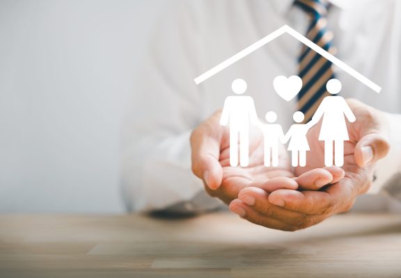 Symbolizing family protection and insurance. Businessman with protective gesture and family silhouette. Icons for family, life, health, and house insurance. Signifying insurance concept.